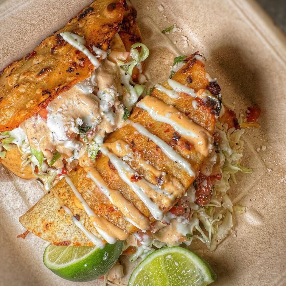 Two Acapela Modern Mex tacos with white and orange sauce, lettuce, and lime wedges.