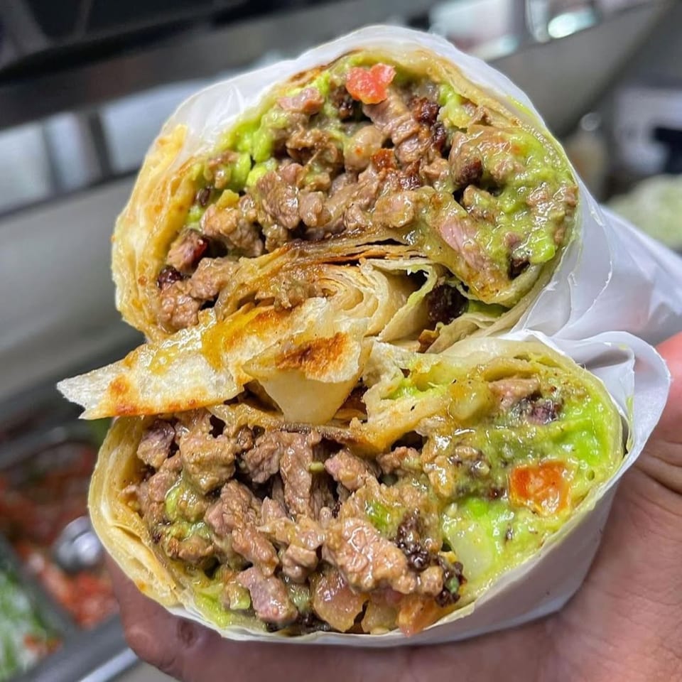 Acapela Modern Mex's carne asada burrito, cut in half, revealing steak, guacamole, and salsa.