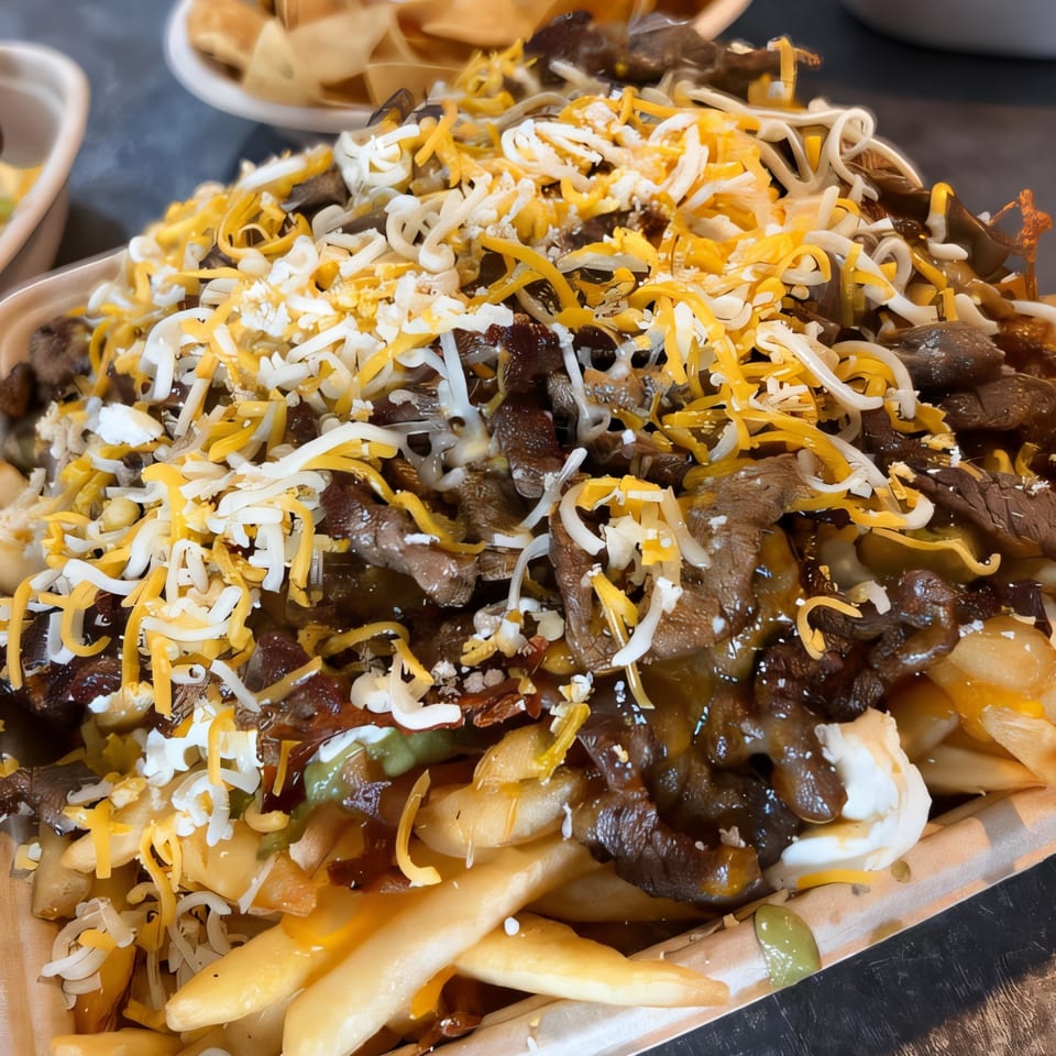 Acapela Modern Mex carne asada fries, topped with shredded cheese, sour cream, and sauce.